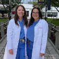 TwomedicalresidentsinwhitecoatsstandtogetheroutsideahospitalentranceonthePCOMcampus