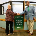 TwoleadersshakehandsbesideanewdirectionalsigninsideaWVSOMHealthfacilityduringaribbon-cuttingordedicationevent