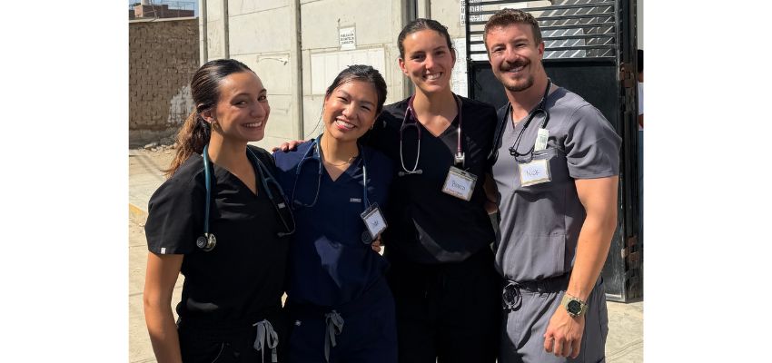 Four medical students wearing scrubs and stethoscopes pose together during an international clinical or service learning experience.