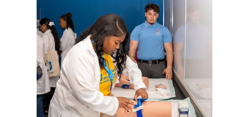 A student practices a clinical procedure on a simulation model during a hands-on skills training session while an instructor observes.