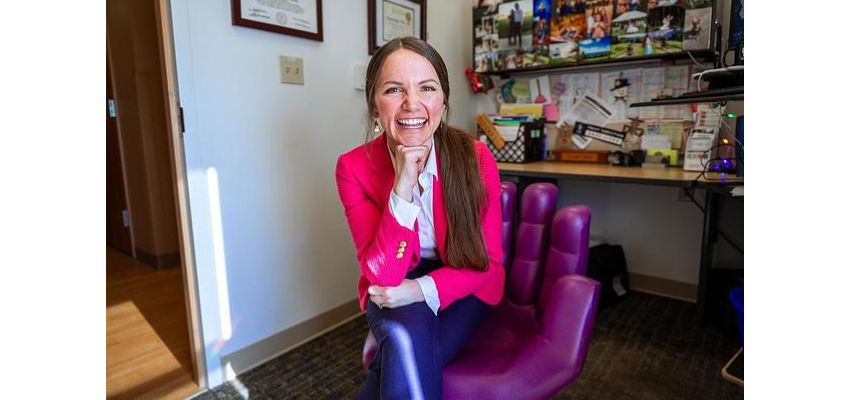 Portrait of a DMUCOM faculty member seated in an office, smiling at the camera.