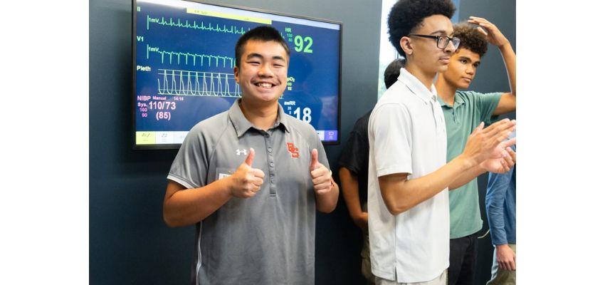 Students participate in a clinical skills demonstration with patient monitoring equipment during a VCOM outreach or educational event.