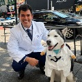 AmedicalstudentkneelsbesideaSiberianHuskywearingawhitedoctorscoatduringacommunityoutreachevent