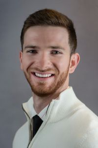 Portrait of a smiling CCOM student wearing a light-colored sweater and tie.