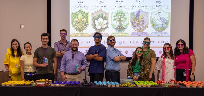 VCOM Louisiana faculty and staff pose behind a table of colorful refreshments during an event celebrating the college's student house system.