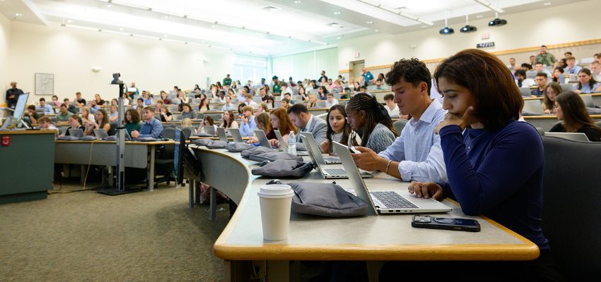 Medical students fill a large lecture hall, working on laptops and taking notes during a class.