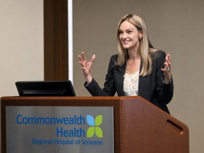 Woman speaking at a podium at Commonwealth Health Regional Hospital of Scranton, gesturing with both hands during a presentation.
