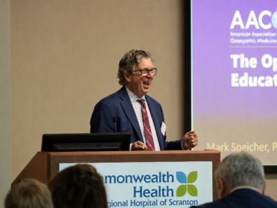 Man speaking and smiling at a podium during an AACOM presentation at Commonwealth Health Regional Hospital of Scranton.