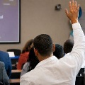 Audiencememberraiseshishandduringapresentationasotherattendeessitfacingthespeaker