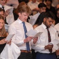 Studentsstandtogetherreadingfromprintedprogramsduringaformalceremony