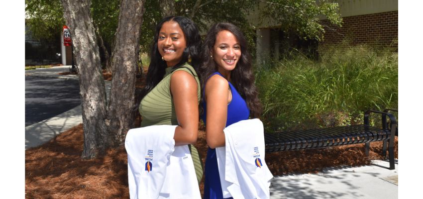 Two medical students pose outdoors holding their new white coats.