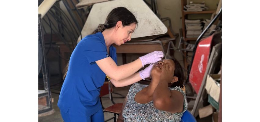 A medical student in blue scrubs examines a patient's eye during a community health outreach visit.