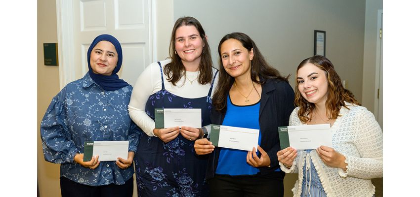 Four students pose together while holding envelopes presented during an awards or recognition event.