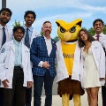 MedicalstudentsinwhitecoatsposewithafacultymemberandtheRowanUniversityowlmascotoutdoors
