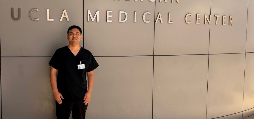 A medical trainee in black scrubs stands in front of a UCLA Medical Center sign.