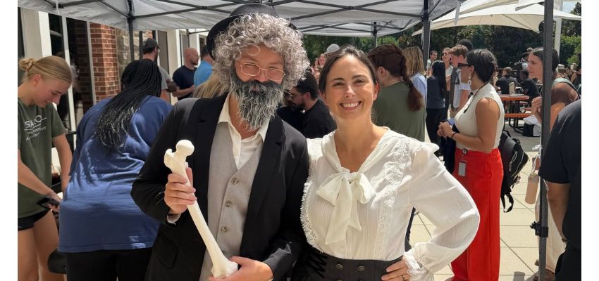 Two people in costume pose together at an outdoor event, with one holding an anatomical model of a leg bone.