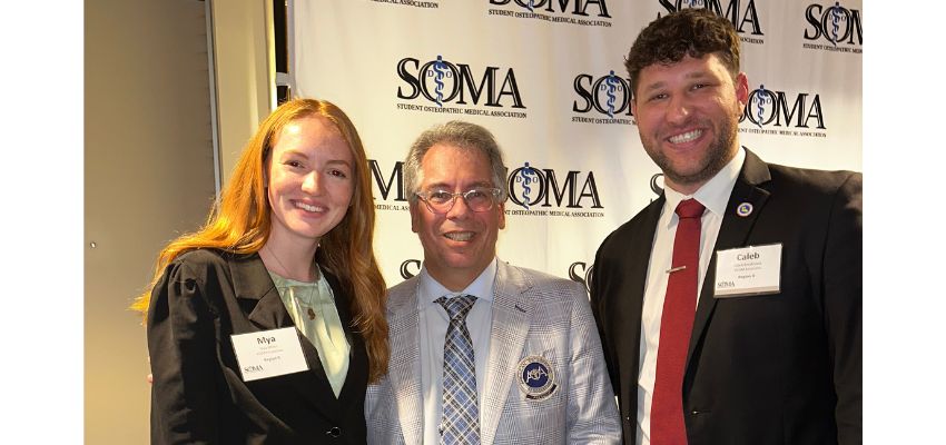 Three attendees pose together in front of a Student Osteopathic Medical Association backdrop at an event.