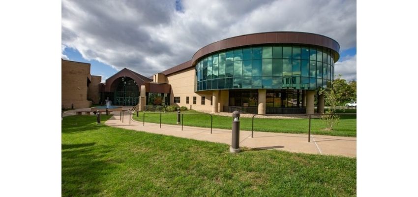 Exterior view of a medical school building featuring a curved glass facade, surrounded by walkways and green lawn.
