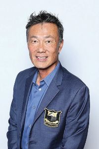 Portrait of a smiling man wearing a blue collared shirt and dark blazer.