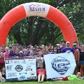 Alargegroupofparticipantsposesoutdoorsbeneathaninflatablearchfollowinganadventureraceevent