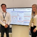 TwostudentsposebesideadigitalresearchposteraboutAIdrivenultrasoundimageacquisitionforechocardiographytraining