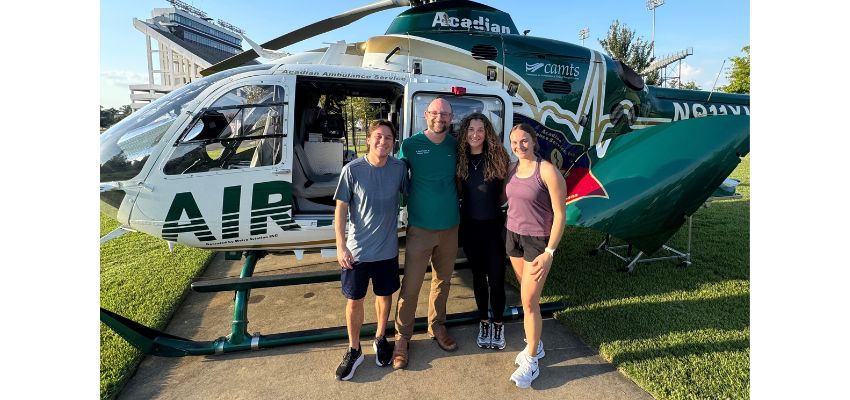 Four people pose in front of an Acadian Air Med medical helicopter outdoors.