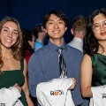 Threestudentsposetogetherataneventwhileholdingfoldedwhitecoats
