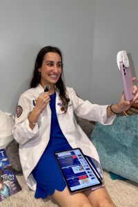 A medical student in a white coat records herself on her iphone.