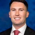 Professionalheadshotofasmilingmanwearingadarksuitandredtie