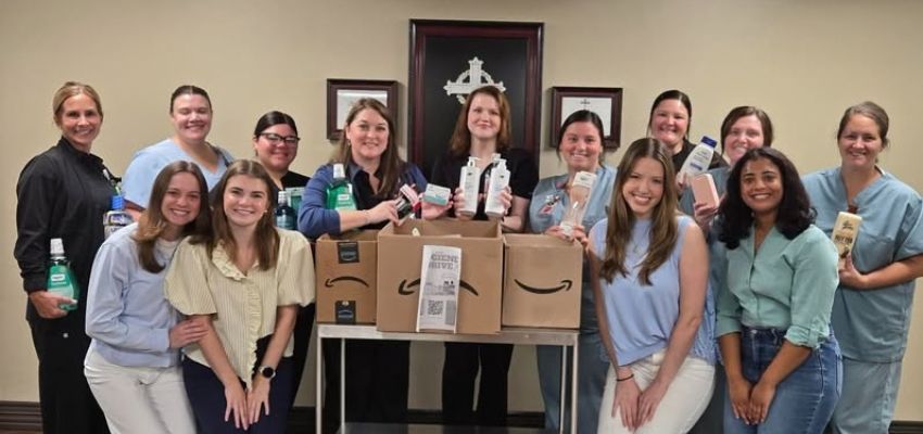 A group of students and medical professionals poses with donated personal care products and boxes collected for a community service project.