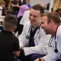 Twomedicalprofessionalsinwhitecoatsspeakwithachildandanadultduringacommunityhealthevent