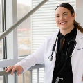 Asmilingphysicianinawhitecoatwithastethoscopeposesbesidealargewindow