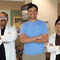 Twomedicalprofessionalsinwhitecoatsposewithamaninablueshirtinsideahealthcarefacility