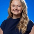 Asmilingwomanwithlongblondehairposesforaprofessionalheadshotagainstabluebackground
