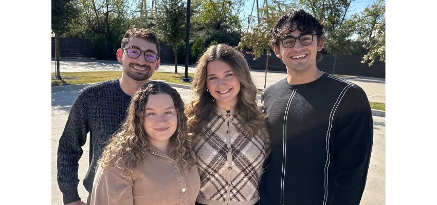 Four smiling medical students pose together outdoors on a sunny day.