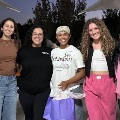 Sixwomenposetogetheratanoutdooreveninggatheringwithseveralholdinggiftbags