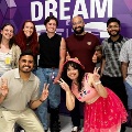 Agroupof11peopleposetogetherinfrontofapurpleDREAMbackdropwithtwoparticipantscrouchinginfrontandmakingpeacesigns