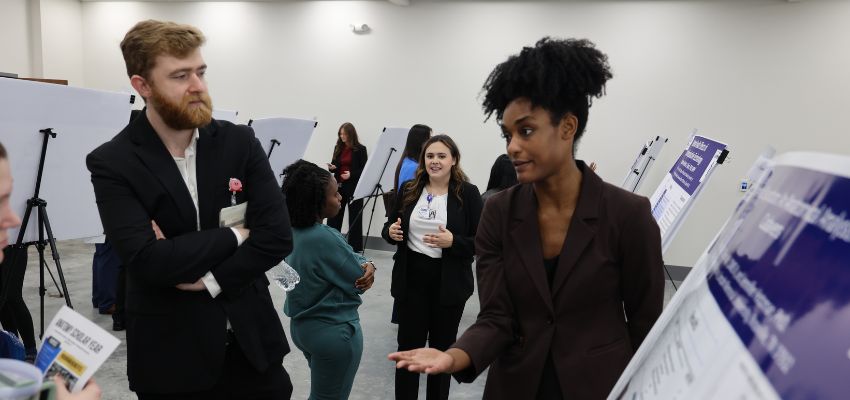 A woman discusses a research poster with a man during an academic poster presentation event.