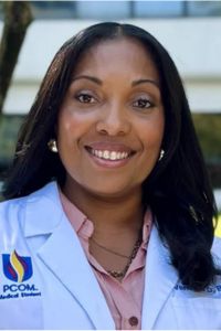 A smiling woman in a white PCOM medical coat poses for a professional headshot.