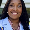 AsmilingwomaninawhitePCOMmedicalcoatposesforaprofessionalheadshot