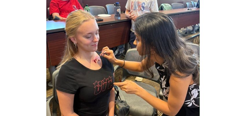 A woman demonstrates a medical procedure on another woman's upper chest during a hands-on educational session.