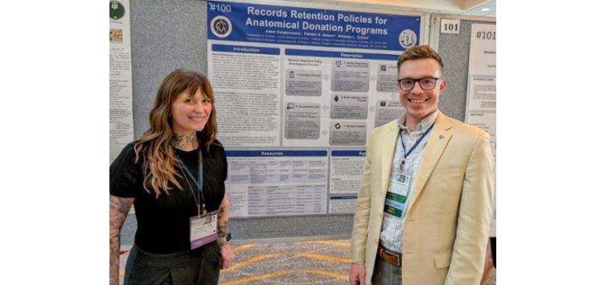 Two LMU-DCOM faculty stand in front of their poster at a conference event.