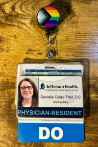 Dr. Thor's hospital ID badge, clipped to a lapel button enamled with the progress flag.