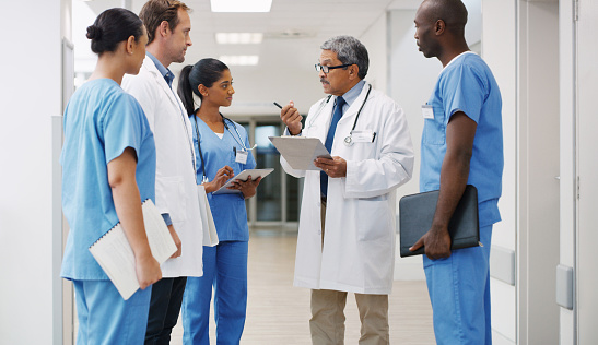 Older doctor discusses a case with younger doctors a hospital hallway