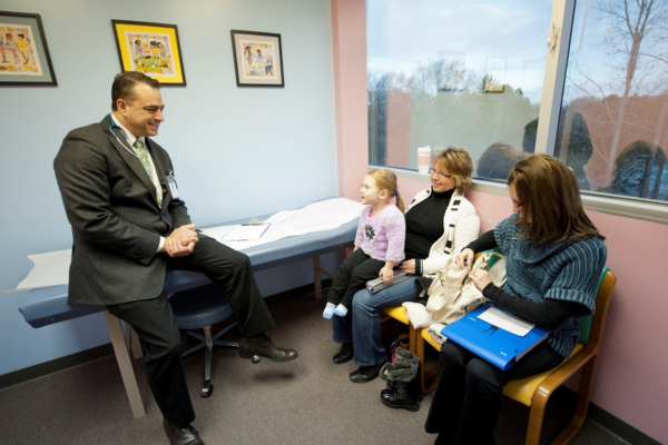 Dr. Amalfitano leaning on a exam table with a pediatric patient and family sitting in chairs across from him