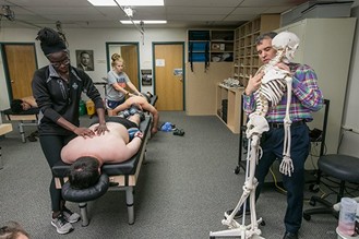 Dr. Degenhardt demonstrating OMM techniques on a skeleton with two students, who are each practicing techniques on people