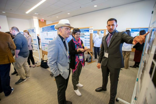 r. Degenhardt at the annual Interdisciplinary Biomedical Research Symposium held on ATSU-COM’s Kirksville campus looking at a poster alongside a woman and man gesturing to the poster