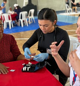 Negia performing a glucose monitoring test on a patient during the Dominican Republic medical outreach trip