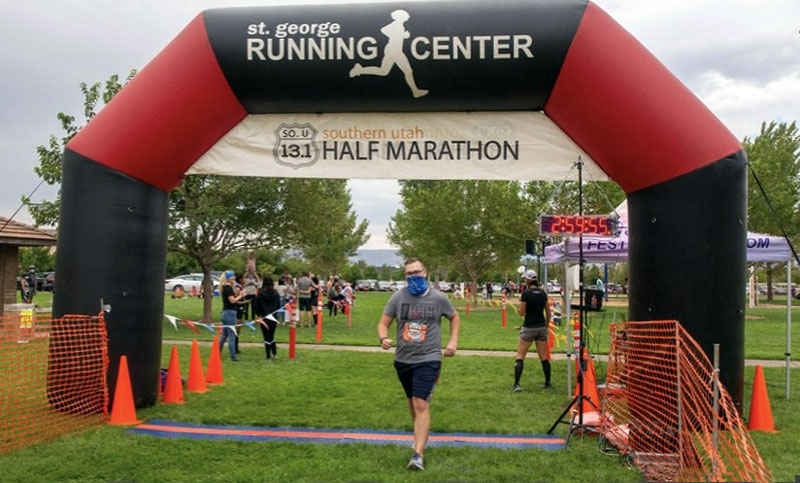 RVUCOM's Kurtis Hinton, wearing face mask, crosses the Southern Utah Half Marathon finish line