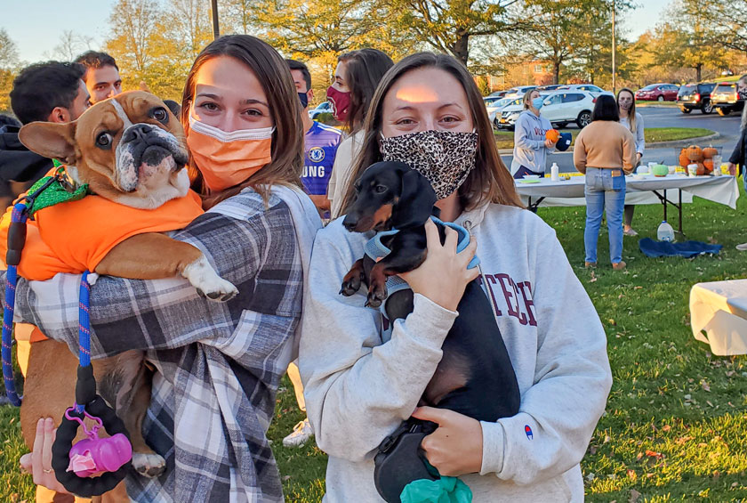 Two female students in masks holding their dogs at VCOM-VC's Harvest Festival